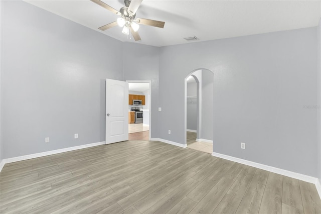 unfurnished bedroom featuring arched walkways, light wood finished floors, baseboards, a walk in closet, and vaulted ceiling