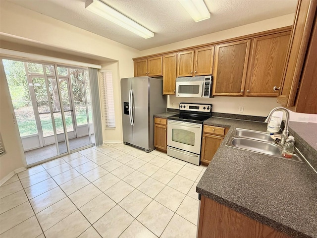 15922 Fishhawk Creek Ln, Lithia, FL 33547 - kitchen featuring appliances with stainless steel finishes, a sink, dark countertops, brown cabinetry, and light tile patterned floors