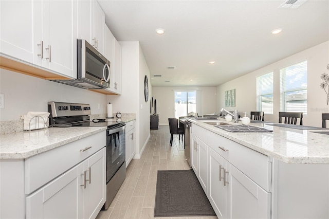 7119 Amelia River Dr, Parrish, FL 34219 - kitchen with stainless steel appliances, a center island with sink, white cabinets, recessed lighting, and light stone counters