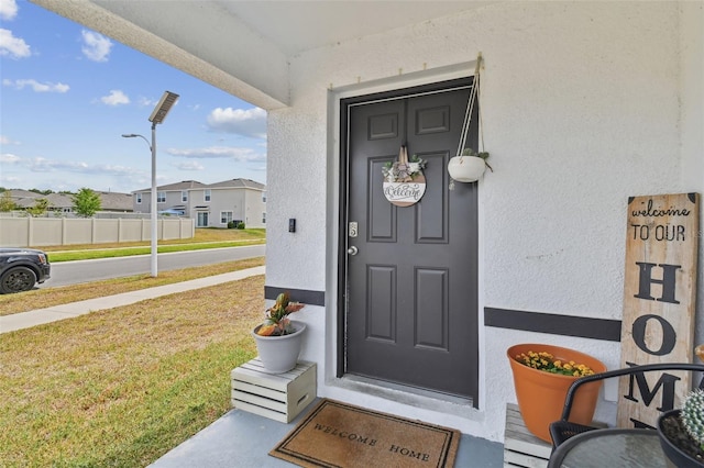 property entrance with stucco siding, a lawn, and a residential view