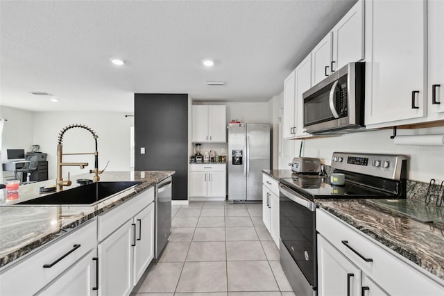 kitchen featuring appliances with stainless steel finishes, a sink, white cabinetry, dark stone counters, and recessed lighting