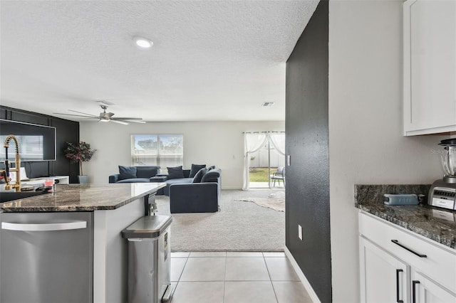 kitchen featuring stainless steel dishwasher, light colored carpet, white cabinets, ceiling fan, and a textured ceiling