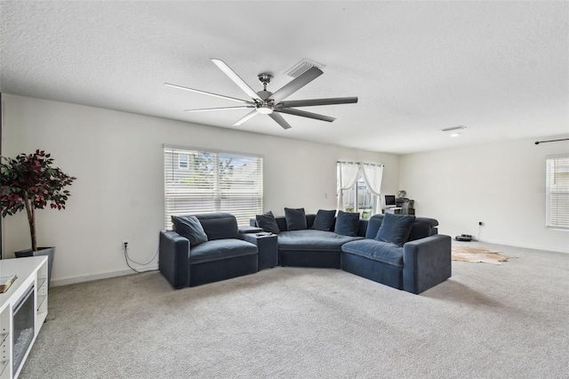 living area featuring a ceiling fan, healthy amount of natural light, a textured ceiling, light colored carpet, and baseboards