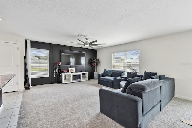 living area featuring a textured ceiling, healthy amount of natural light, a ceiling fan, light tile patterned flooring, and light colored carpet