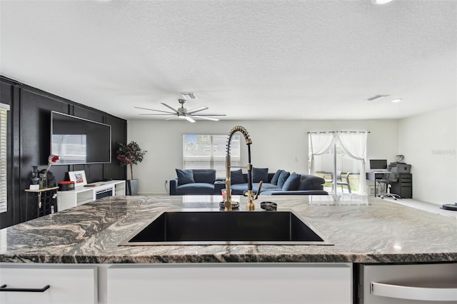 kitchen with a sink, open floor plan, dark stone countertops, healthy amount of natural light, and a textured ceiling