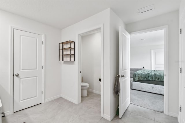 ensuite bathroom with toilet, baseboards, and tile patterned flooring