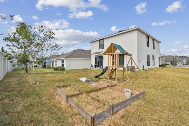 back of house featuring a playground, a lawn, a vegetable garden, and stucco siding