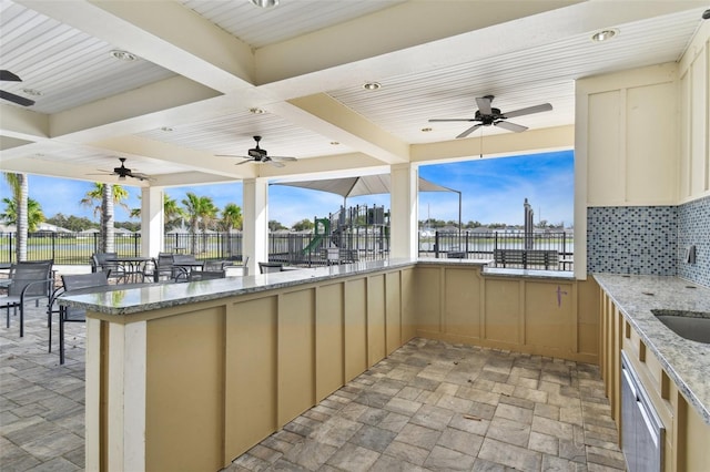 view of patio with ceiling fan, a water view, and a bar