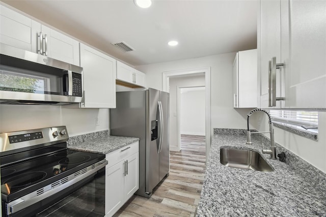 kitchen with appliances with stainless steel finishes, a sink, light wood-type flooring, white cabinets, and recessed lighting