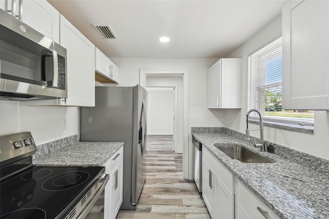 kitchen featuring appliances with stainless steel finishes, a sink, light wood-style flooring, white cabinets, and recessed lighting