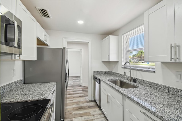 kitchen with appliances with stainless steel finishes, a sink, light wood-style flooring, white cabinets, and recessed lighting