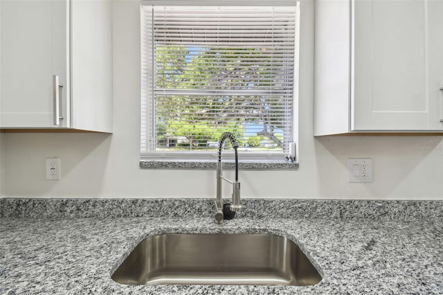 kitchen view of a sink, white cabinetry, and light stone countertops