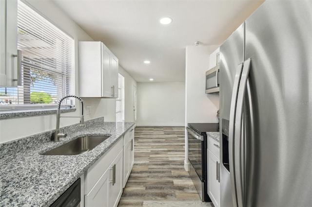 kitchen with appliances with stainless steel finishes, a sink, wood finished floors, white cabinetry, and recessed lighting