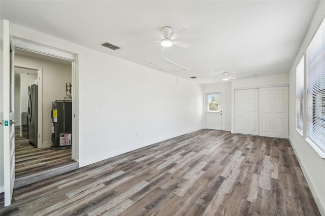 spare room with attic access, electric water heater, ceiling fan, wood finished floors, and baseboards