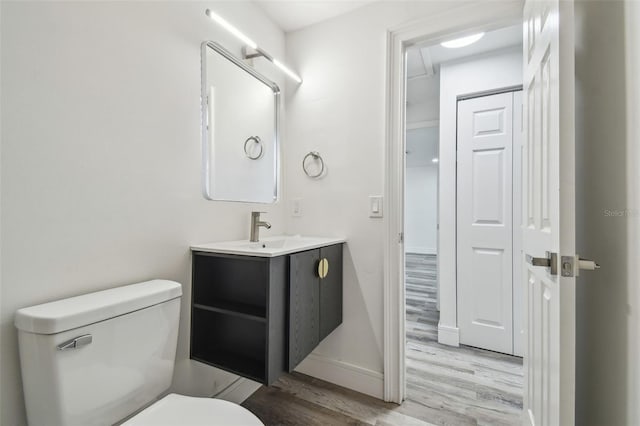 half bath with wood finished floors, toilet, vanity, and baseboards