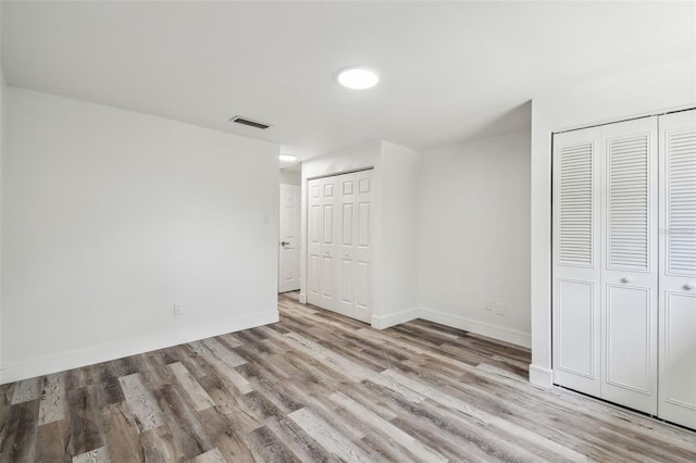 unfurnished bedroom with multiple closets, wood finished floors, and baseboards