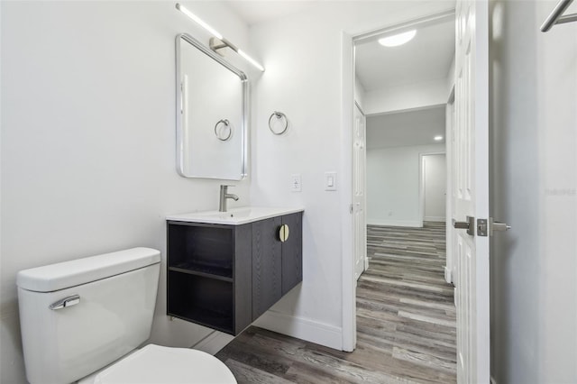 half bathroom with wood finished floors, toilet, baseboards, and vanity