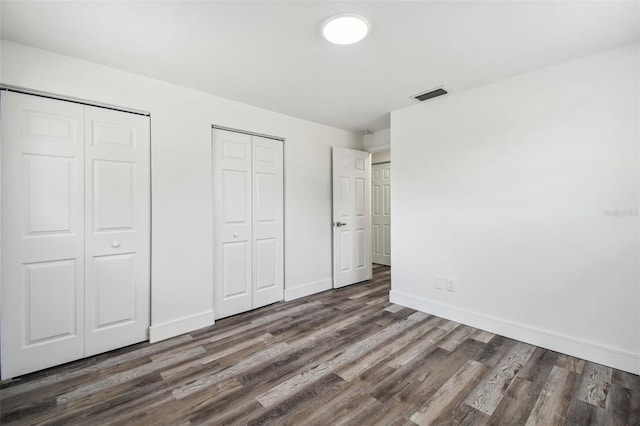 unfurnished bedroom with two closets, wood finished floors, and baseboards