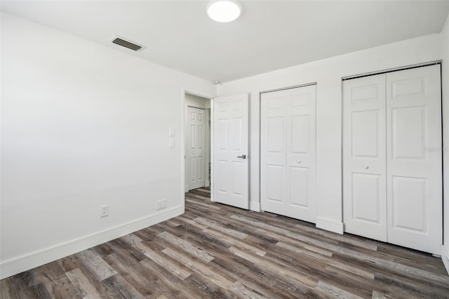 unfurnished bedroom with wood finished floors, multiple closets, and baseboards