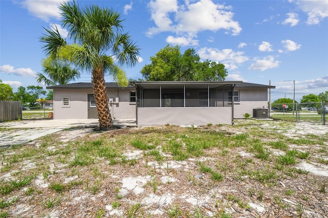 rear view of house with central AC, a sunroom, stucco siding, and a gate