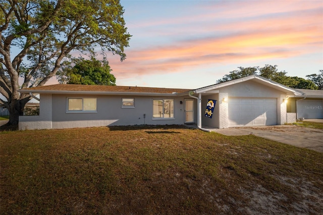 ranch-style house featuring a garage, concrete driveway, a front lawn, brick siding, and stucco siding