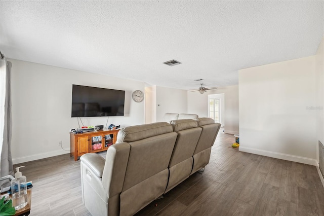 living room with a textured ceiling, wood finished floors, baseboards, and a ceiling fan