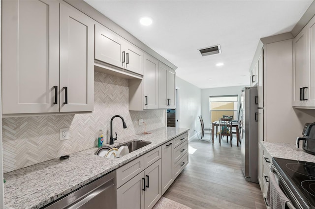 kitchen featuring a sink, stainless steel appliances, backsplash, light stone countertops, and light wood-type flooring