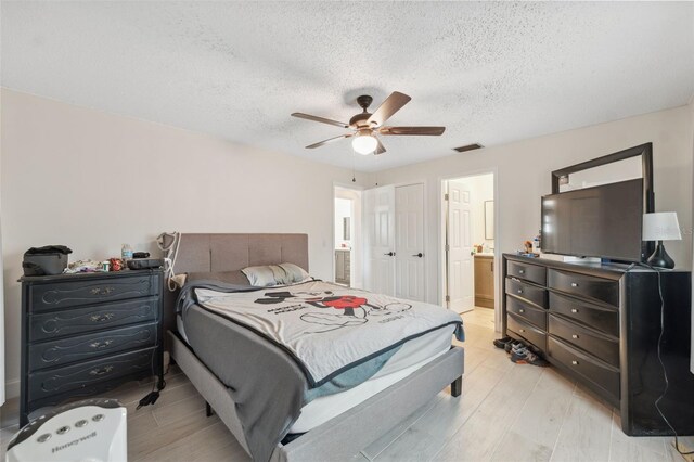 bedroom featuring ensuite bathroom, a textured ceiling, light wood-style flooring, and ceiling fan
