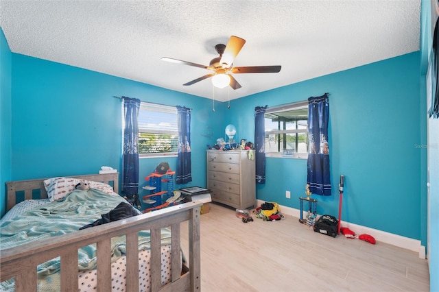 bedroom with multiple windows, wood finished floors, a textured ceiling, baseboards, and ceiling fan