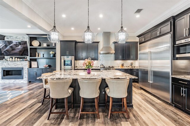 17724 Daisy Farm Dr, Lutz, FL 33559 - kitchen with appliances with stainless steel finishes, wall chimney range hood, a center island with sink, light stone countertops, and a kitchen bar