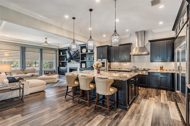 17724 Daisy Farm Dr, Lutz, FL 33559 - kitchen featuring wall chimney range hood, stainless steel appliances, a kitchen island with sink, light stone counters, and a kitchen breakfast bar