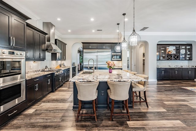 17724 Daisy Farm Dr, Lutz, FL 33559 - kitchen featuring stainless steel appliances, arched walkways, wall chimney range hood, backsplash, and light stone counters