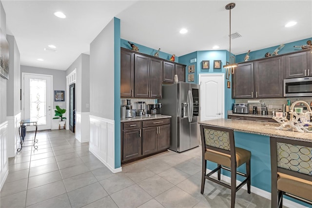 11684 Brighton Knoll Loop, Riverview, FL 33579 - kitchen with stainless steel appliances, dark brown cabinetry, light stone counters, a breakfast bar area, and a wainscoted wall