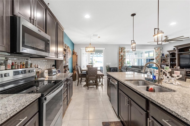 11684 Brighton Knoll Loop, Riverview, FL 33579 - kitchen with appliances with stainless steel finishes, a sink, dark brown cabinets, open floor plan, and light stone counters