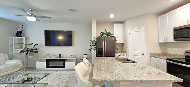 kitchen with appliances with stainless steel finishes, a sink, open floor plan, white cabinetry, and light stone countertops