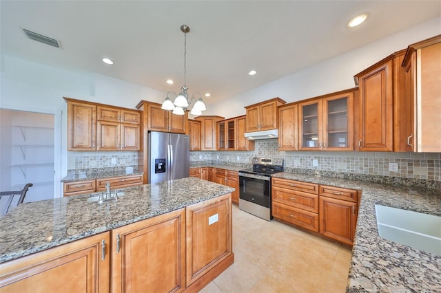 710 116th Ave, Treasure Island, FL 33706 - kitchen featuring stainless steel appliances, under cabinet range hood, brown cabinetry, dark stone counters, and a chandelier