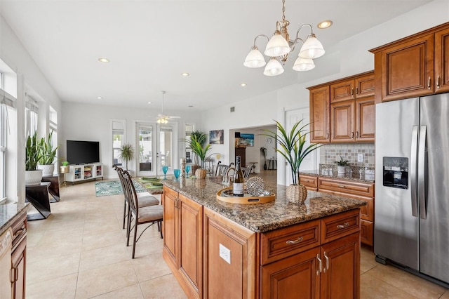 710 116th Ave, Treasure Island, FL 33706 - kitchen with stainless steel fridge with ice dispenser, light tile patterned floors, dark stone countertops, brown cabinets, and ceiling fan