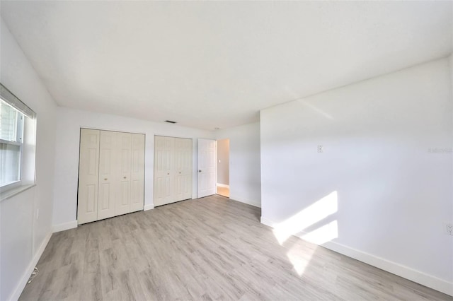 710 116th Ave, Treasure Island, FL 33706 - unfurnished bedroom featuring multiple closets, light wood-style flooring, and baseboards