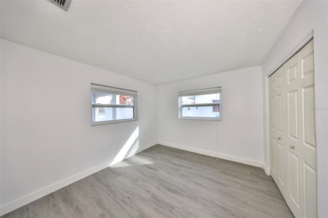 710 116th Ave, Treasure Island, FL 33706 - unfurnished bedroom with multiple windows, baseboards, wood finished floors, a closet, and a textured ceiling