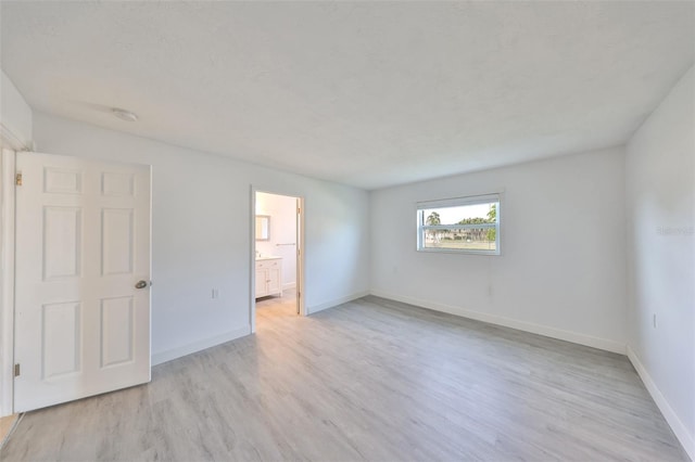710 116th Ave, Treasure Island, FL 33706 - unfurnished bedroom with light wood-type flooring, baseboards, and connected bathroom