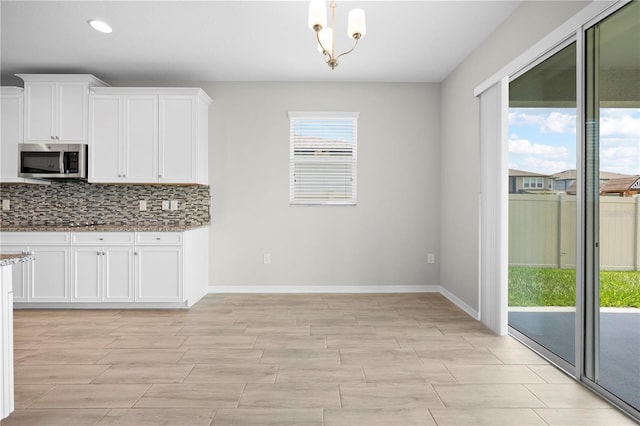 17618 Cortes Creek Blvd, Spring Hill, FL 34610 - kitchen featuring stainless steel microwave, light stone countertops, white cabinets, baseboards, and wood tiled floors