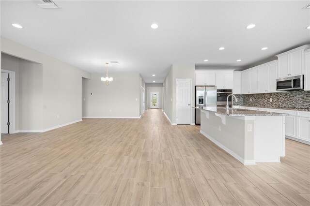 17618 Cortes Creek Blvd, Spring Hill, FL 34610 - kitchen with appliances with stainless steel finishes, a chandelier, a center island with sink, light wood-style floors, and backsplash