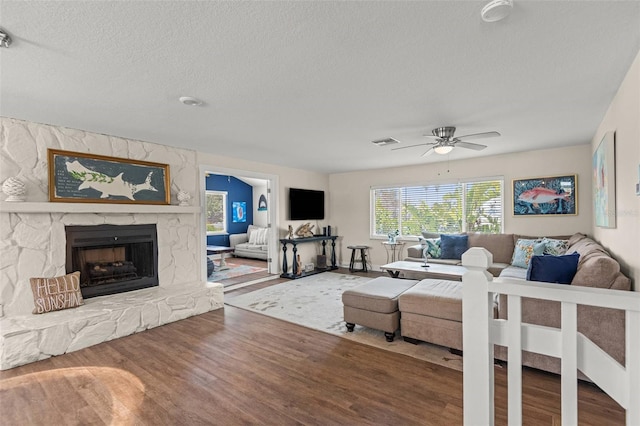 1210 Bay Pine Blvd, Indian Rocks Beach, FL 33785 - living room featuring wood finished floors, a textured ceiling, a stone fireplace, and ceiling fan
