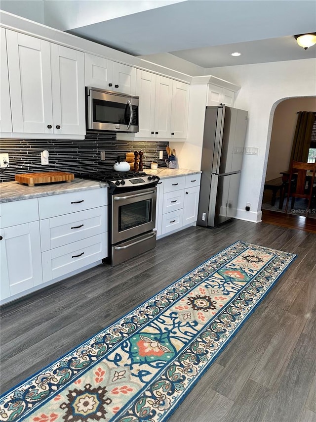 1020 38th Ave N, Saint Petersburg, FL 33704 - kitchen with stainless steel appliances, dark wood-type flooring, arched walkways, white cabinetry, and backsplash