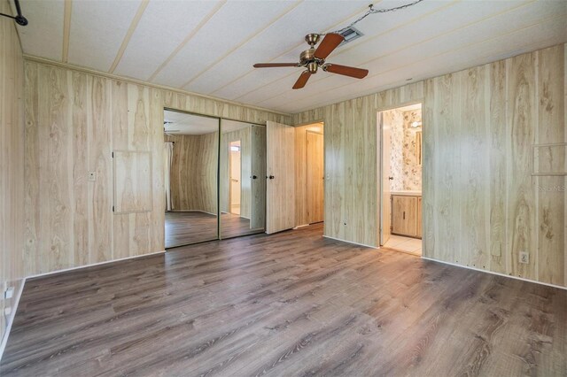 3542 Castle Dr, Zephyrhills, FL 33540 - unfurnished bedroom featuring wood walls, wood finished floors, ensuite bathroom, a closet, and a ceiling fan