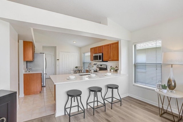 4921 Wessex Way, Land O Lakes, FL 34638 - kitchen featuring appliances with stainless steel finishes, lofted ceiling, a sink, brown cabinetry, and a breakfast bar