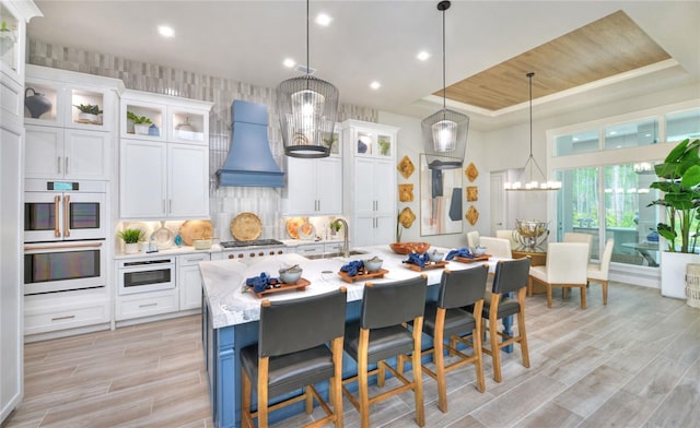 256 Stirling Bridge Dr, Ormond Beach, FL 32174 - kitchen with premium range hood, a tray ceiling, white appliances, a kitchen bar, and white cabinetry