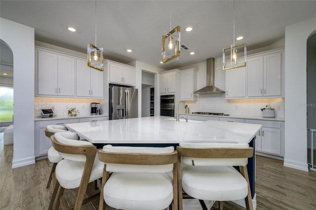 3952 Aldea Way, Wesley Chapel, FL 33543 - kitchen with wall chimney exhaust hood, appliances with stainless steel finishes, backsplash, dark wood-style flooring, and a center island with sink