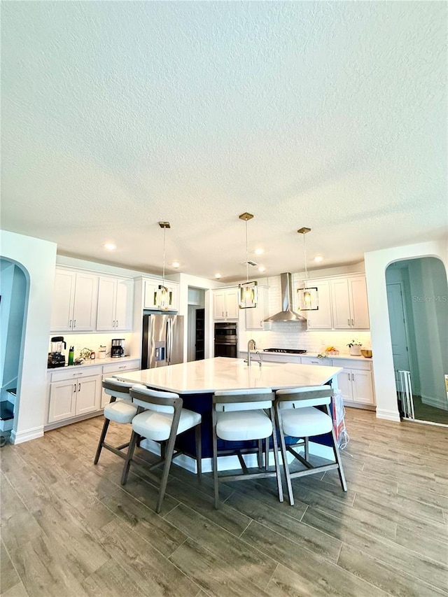 3952 Aldea Way, Wesley Chapel, FL 33543 - kitchen featuring stainless steel fridge, wall chimney exhaust hood, arched walkways, a textured ceiling, and white cabinets