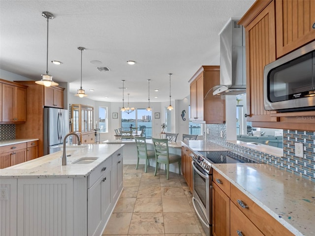 11000 8th St E, Treasure Island, FL 33706 - kitchen with stainless steel appliances, wall chimney range hood, decorative backsplash, a kitchen island with sink, and light stone countertops